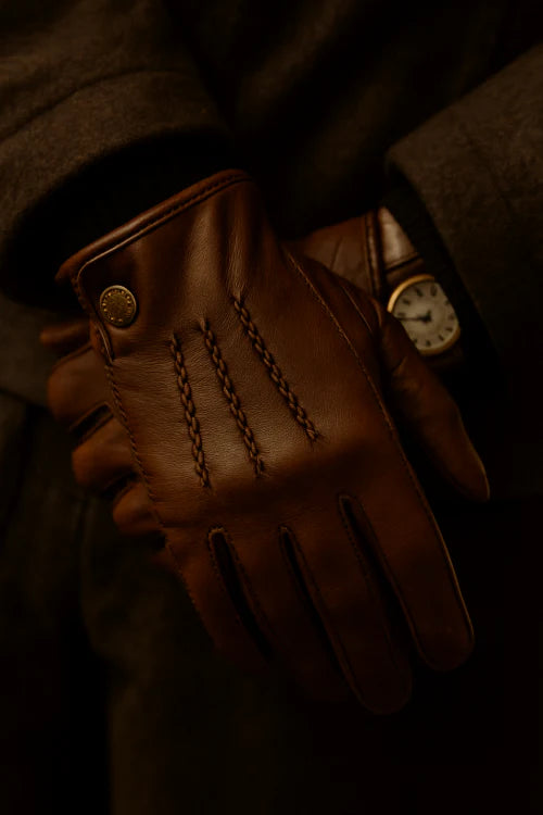 Paire de gants vintage en cuir marron posée sur une veste élégante, éclairage chaleureux pour ambiance rétro chic.