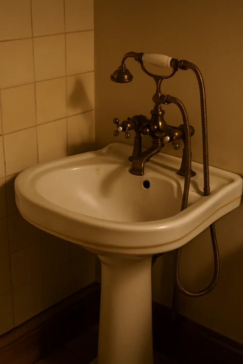 Meuble lavabo rétro en céramique blanche avec robinet ancien en laiton dans une salle de bain vintage chaleureuse